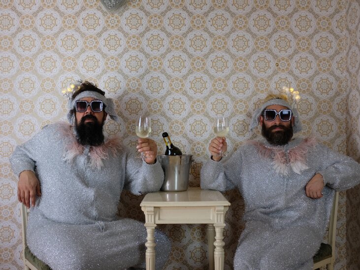 Zwei Männer in glitzernden Anzügen stoßen mit Sektgläsern an. | © Thomas Galli-Magerl