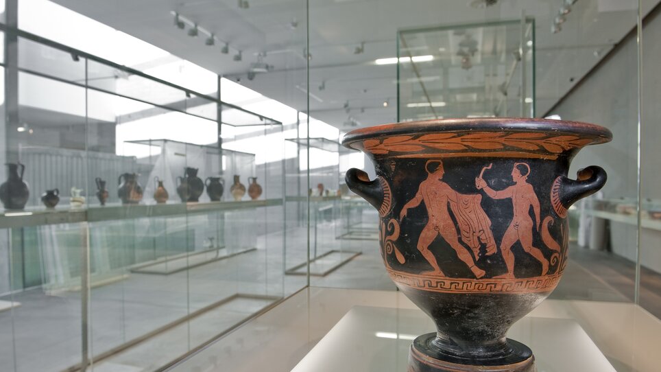Eine antike griechische Vase mit Figuren in einem Ausstellungsraum. | © UMJ - N. Lackner