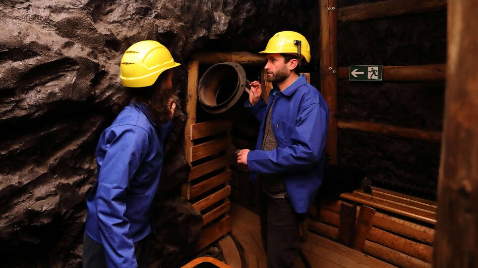 Zwei Personen in Schutzkleidung in einem Schacht, beobachten eine Apparatur. | © Universalmuseum Joanneum - J. Kucek