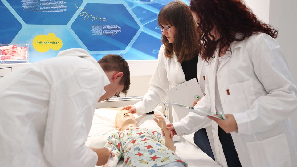 Three individuals practice on a medical training mannequin in a training facility. | © Universalmuseum Joanneum - J. Kucek