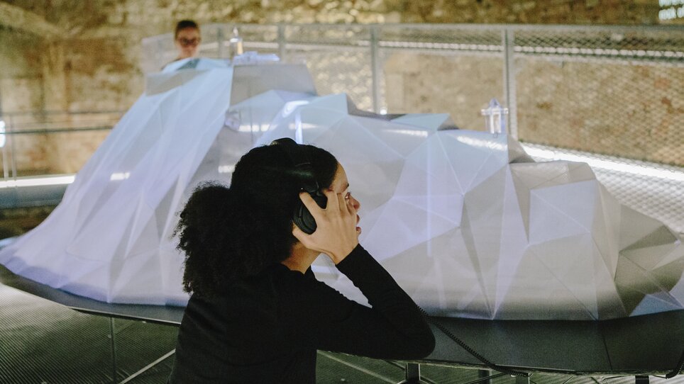 Visitor wearing headphones in an exhibition with a 3D object. | © Sebastian Reiser