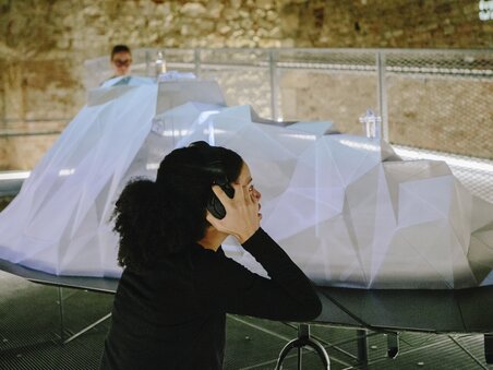 Besucherin mit Kopfhörern in einer Ausstellung mit einem 3D-Objekt. | © Sebastian Reiser