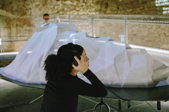 Besucherin mit Kopfhörern in einer Ausstellung mit einem 3D-Objekt. | © Sebastian Reiser