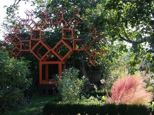 A creative garden featuring a striking orange tree design made of geometric shapes. | © kunstGarten