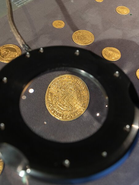 Golden coins displayed in the exhibit, illuminated from above. | © Universalmuseum Joanneum - N. Lackner