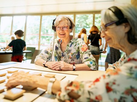 Two elderly women with headphones playing at a table.