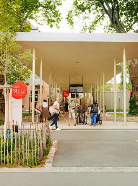 Visitors at Salon Stolz, a modern building in a park with trees.