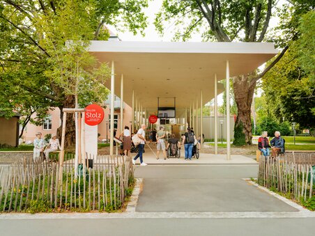 Visitors at Salon Stolz, a modern building in a park with trees.