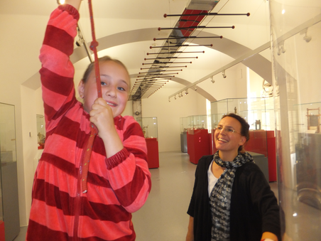 Ein Mädchen spielt in einem Museum, während eine Frau lächelt. | © UniGraz@Museum