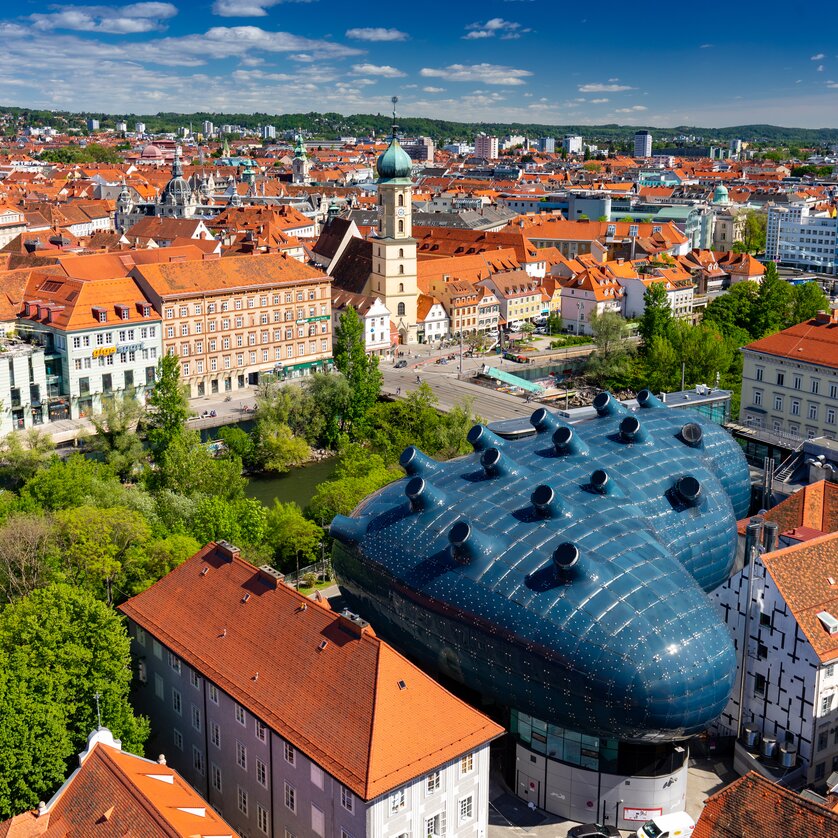 Blick auf Graz mit dem blauen Kunsthaus zwischen historischen Dächern. | © Graz Tourismus - Harry Schiffer