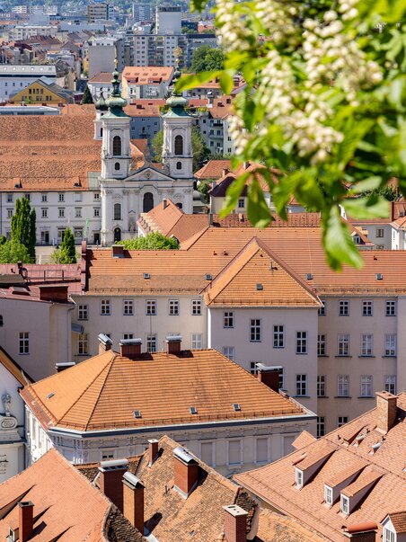 Blick über Graz mit der roten Dachlandschaft und der Mariahilferkirche im Hintergrund. | © Graz Tourismus - Harry Schiffer