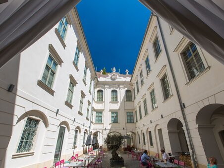Ein Blick in einen Innenhof mit Cafés, einem Baum und strahlend blauem Himmel in Graz. | © Graz Tourismus - Harry Schiffer