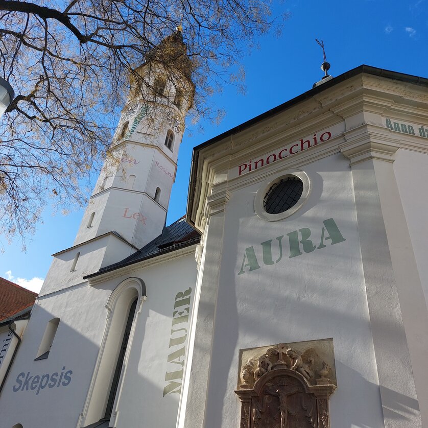 White exterior façade of the Andrä Church with the inscriptions "Aura" and "Pinocchio". | © Graz Tourismus - Information