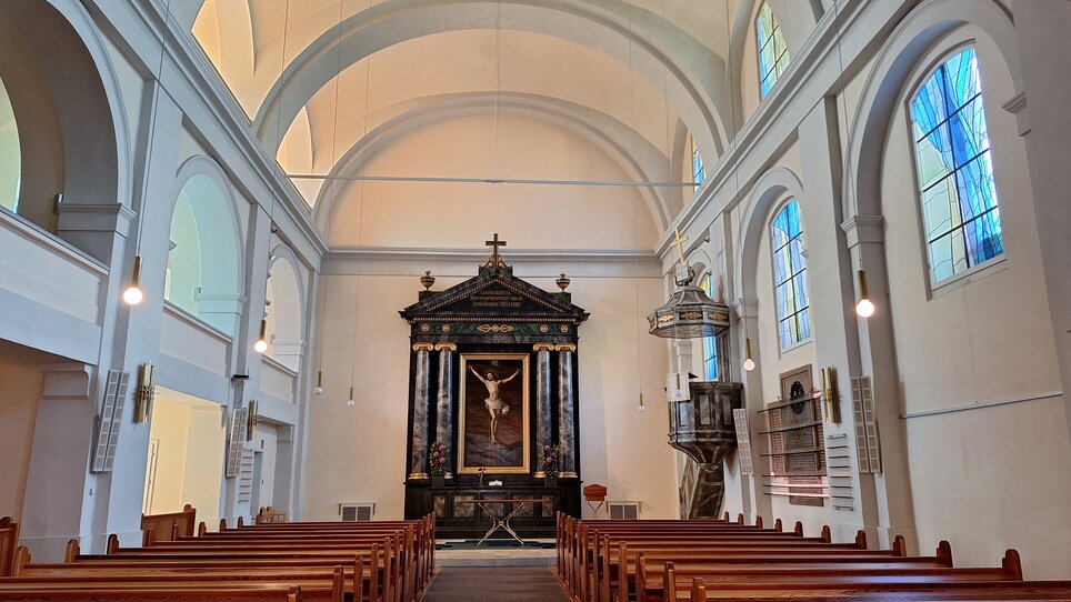 The interior features wooden pews and an altar displaying a crucifixion. | © Graz Tourismus - Doris Pucher
