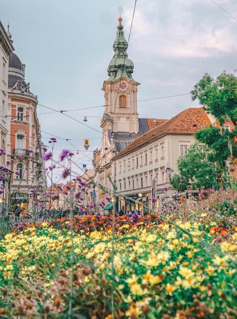 View of the City Parish Church in Graz with flowers in the foreground. | © Janet Newenham - Journalist On The Run