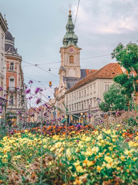 View of the City Parish Church in Graz with flowers in the foreground. | © Janet Newenham - Journalist On The Run
