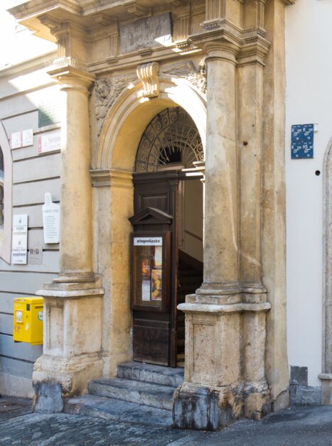 View of the LAURA shop with red windows, next to it is the entrance to the Stiegenkirche in Graz. | © Graz Tourismus - Harry Schiffer