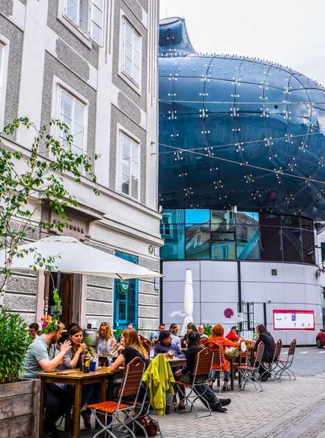 View of Kunsthaus Graz and a street café with guests. | © Becki Enright_Boarders of Adventure