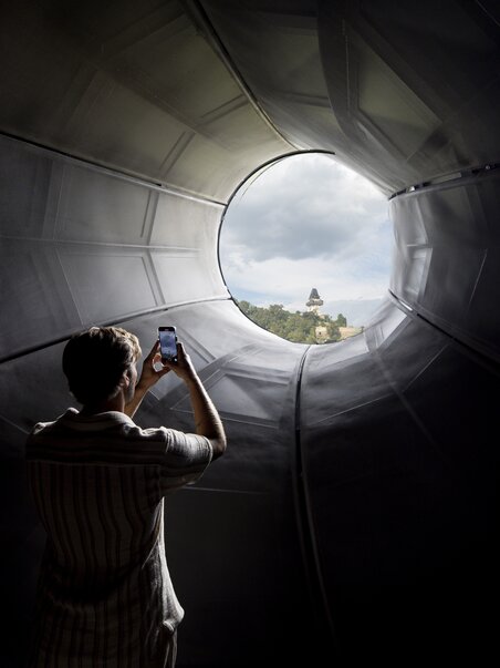Visitor photographs Graz Clock Tower through Kunsthaus Graz. | © Graz Tourismus - Tom Lamm