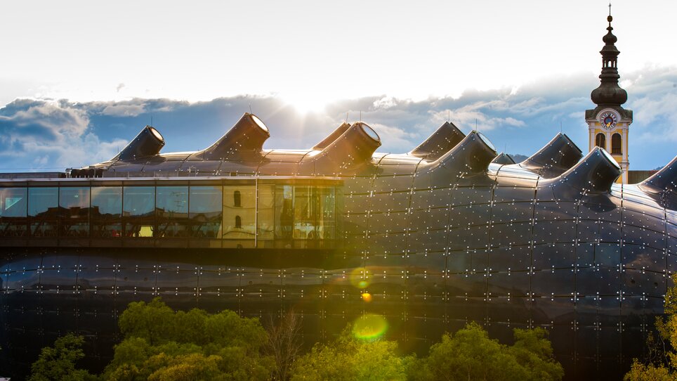 Das Kunsthaus Graz mit einem Kirchturm im Hintergrund. | © Graz Tourismus - Harry Schiffer