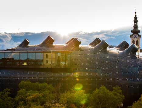 Das Kunsthaus Graz mit einem Kirchturm im Hintergrund. | © Graz Tourismus - Harry Schiffer