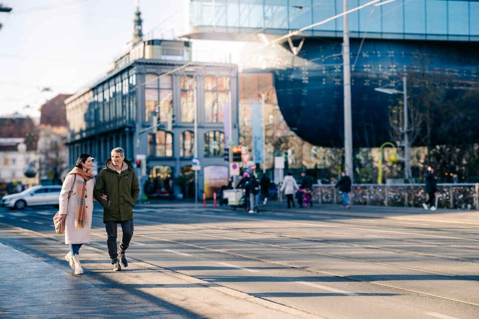 Ein Paar geht an einem sonnigen Tag vor dem Kunsthaus Graz spazieren. | © Graz Tourismus - Mias Photoart