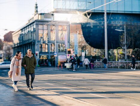 Ein Paar geht an einem sonnigen Tag vor dem Kunsthaus Graz spazieren. | © Graz Tourismus - Mias Photoart