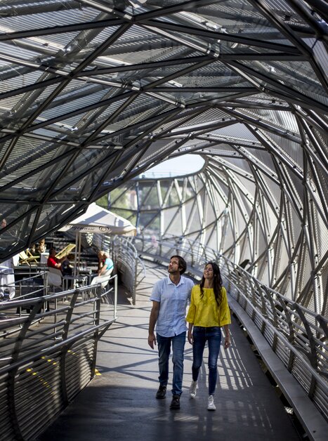 Ein Paar spaziert über die Murinsel in Graz, umgeben von einer modernen Architektur. | © Graz Tourismus - Tom Lamm