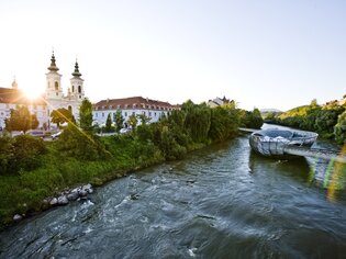 Blick auf die Murinsel in Graz, umgeben von Bäumen und historischen Gebäuden.