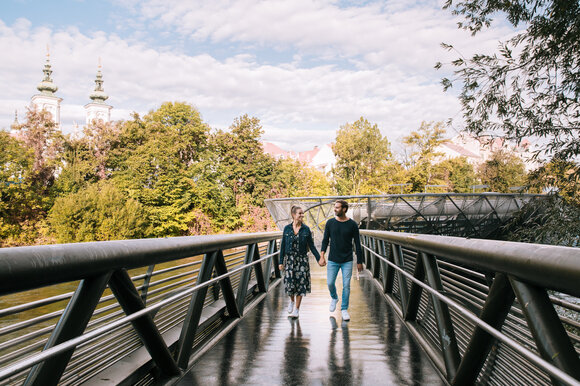 Paar spaziert auf der Murinsel in Graz, umgeben von Bäumen. | © Graz Tourismus