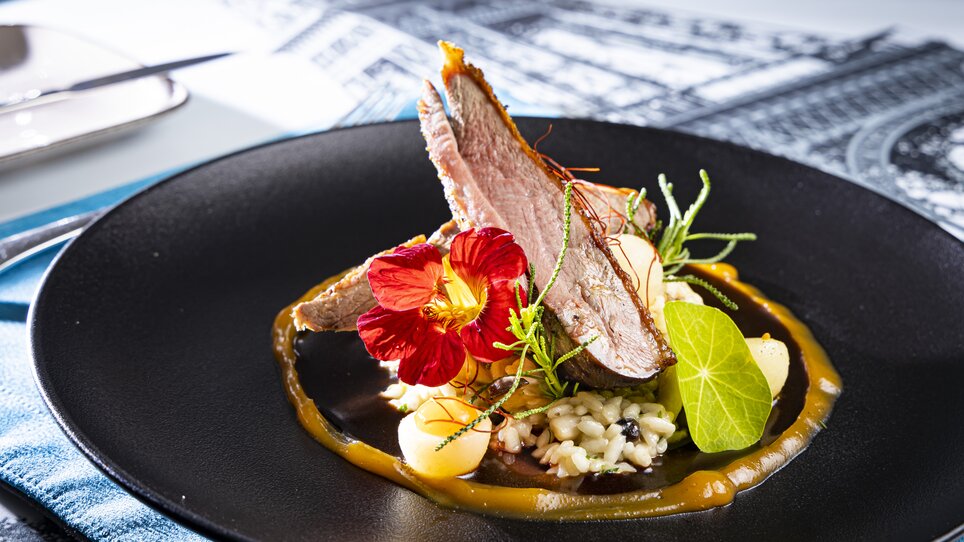 An artistic dish with meat, flowers, and risotto on a black plate. | © Graz Tourismus - Werner Krug