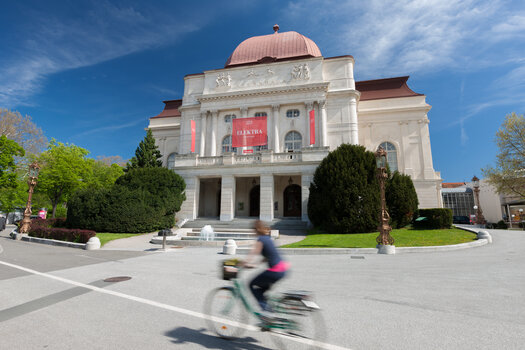 Die Oper Graz mit lebendigem Umfeld und einem Radfahrer auf der Straße. | © Graz Tourismus - Harry Schiffer