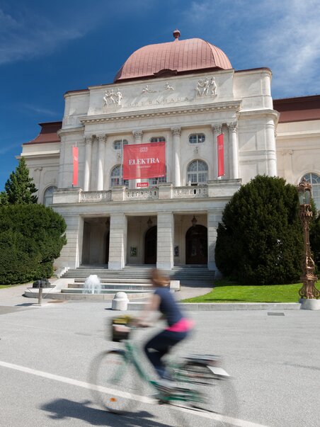 L'Opera Graz con un ambiente vivace e un ciclista sul marciapiede. | © Graz Tourismus - Harry Schiffer