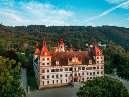 A view of Eggenberg Palace, surrounded by trees and mountains. | © Graz Tourismus - Mias Photoart