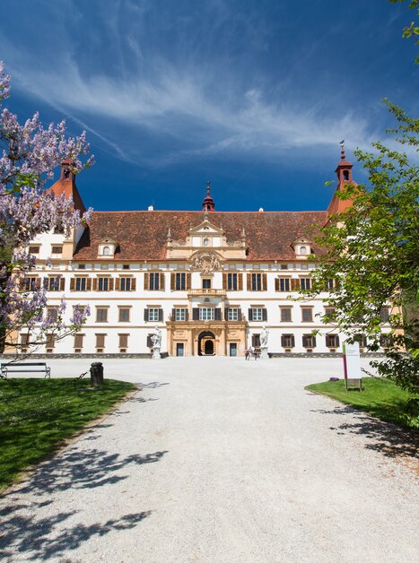 Schloss Eggenberg in Graz, umgeben von blühenden Bäumen und klarem Himmel. | © Graz Tourismus - Harry Schiffer