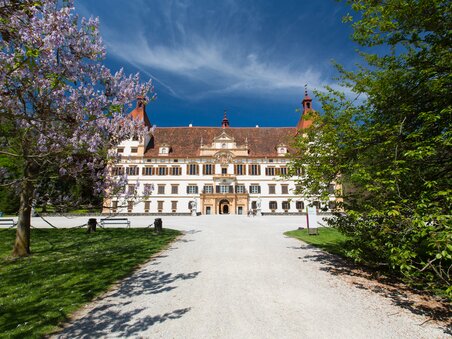 Eggenberg Palace in Graz, surrounded by blooming trees and a clear sky. | © Graz Tourismus - Harry Schiffer