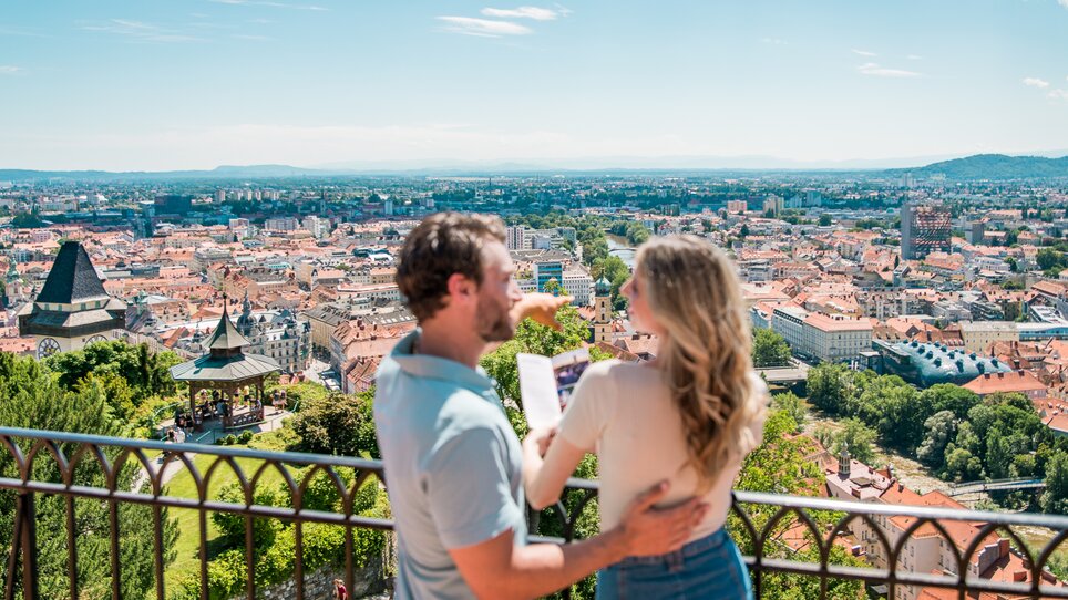 Couple enjoying the view of Graz from the Schlossberg. The two are looking at a brochure of Graz. | © Graz Tourismus - Mias Photoart