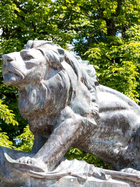 Bronze lion sculpture on Schlossberg in Graz with green trees. | © Graz Tourismus - Harry Schiffer