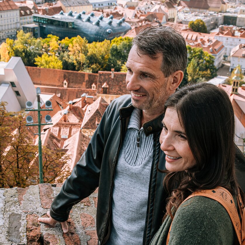 Couple Enjoying View over Graz | © Graz Tourismus A couple enjoys the view over Graz. In the background, the Kunsthaus and the beautiful red rooftop landscape can be seen. | © Graz Tourismus