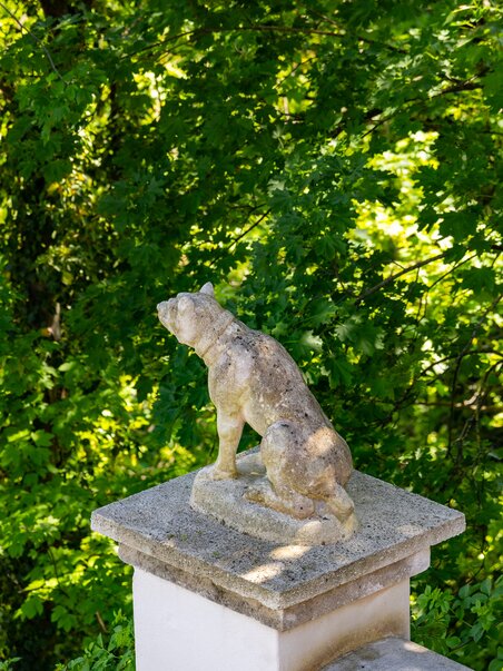 Eine steinerne Hundeskulptur vor einer grünen Baumkulisse. | © Graz Tourismus - Harry Schiffer