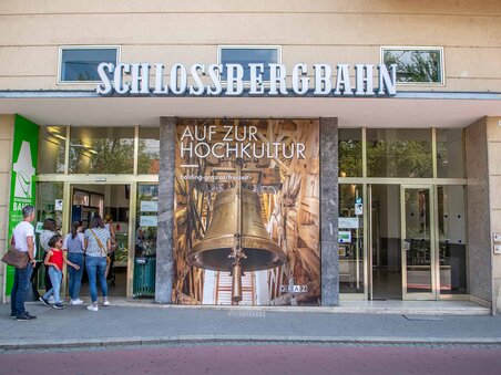 Entrance to the Schlossberg Funicular in Graz with a poster and visitors. | © achtzigzehn - Hinterleitner