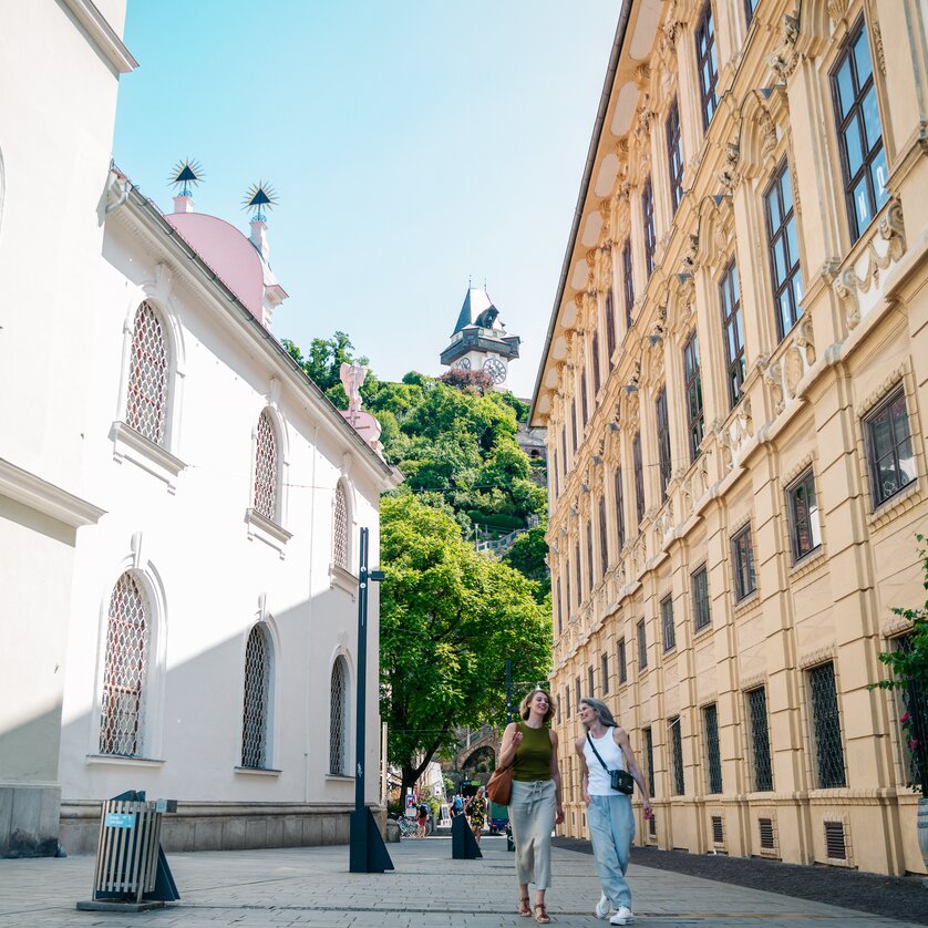 Two women walking at Schlossbergplatz in Graz, Clock Tower in the background. | © Graz Tourismus - Mias Photoart