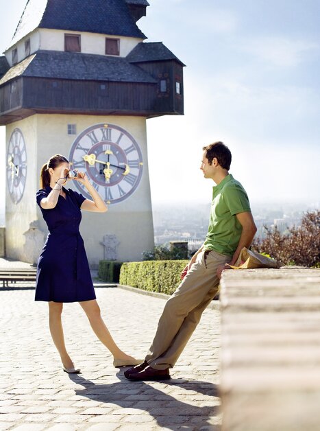 Ein Paar posiert am Grazer Uhrturm und genießt die Aussicht über Graz. | © Graz Tourismus - Gerhard  Wasserbauer