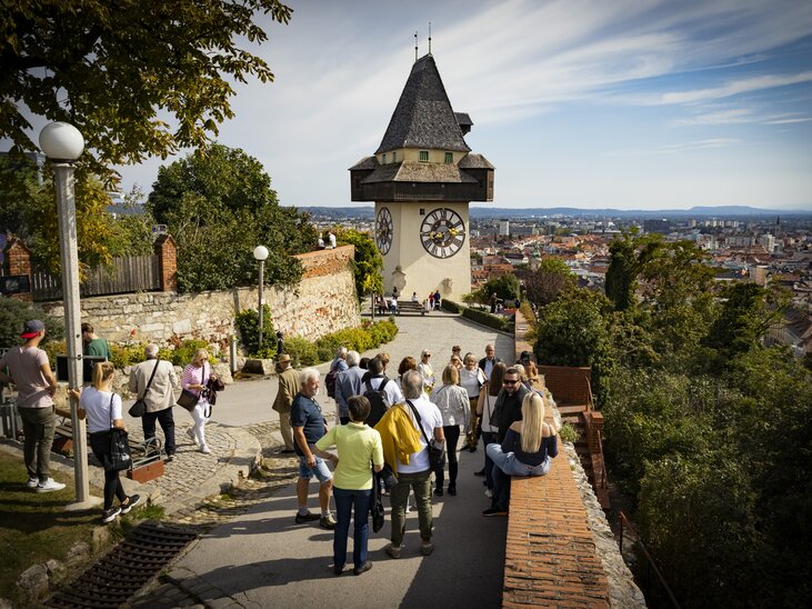Visitors exploring the Schlossberg with a view of the Graz Clock Tower and the city. | © Graz Tourismus - Werner Krug