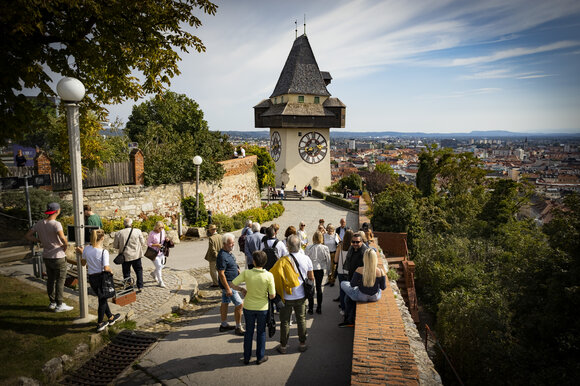 Visitors exploring the Schlossberg with a view of the Graz Clock Tower and the city. | © Graz Tourismus - Werner Krug