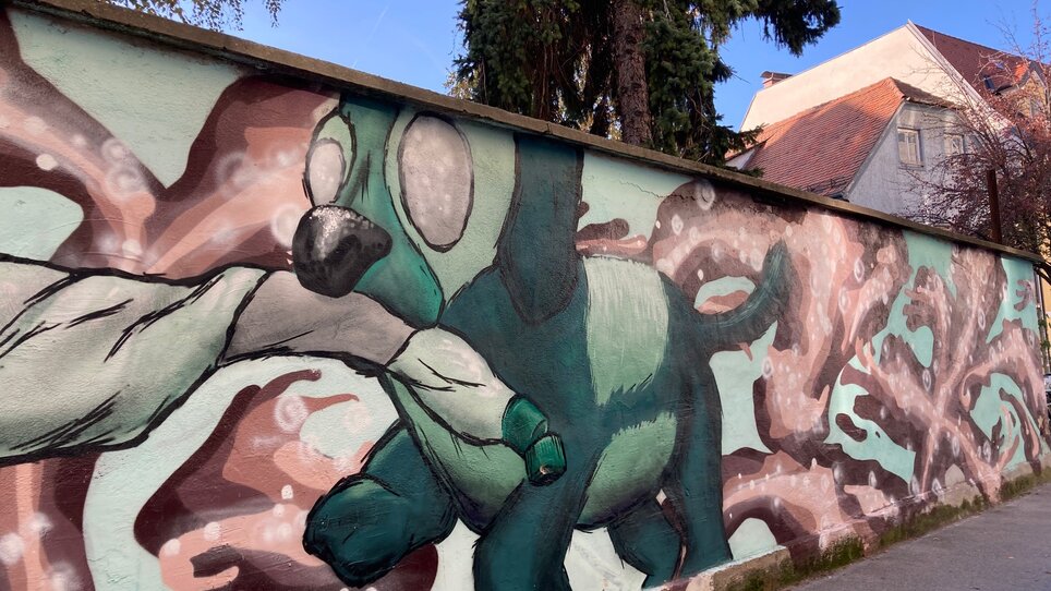 Ein farbenfrohes Graffiti mit einem Hund, der ein Spielzeug trägt. | © Graz Tourismus - NA