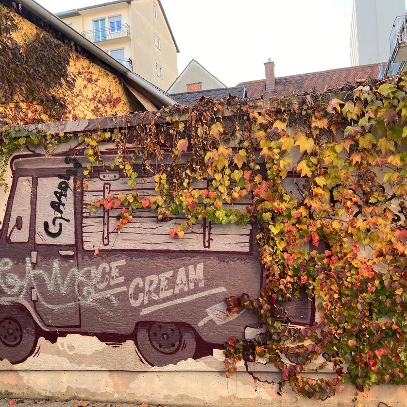 Un graffito di un carrello gelato coperto di foglie colorate. | © Graz Tourismus - NA