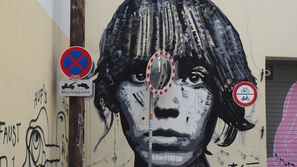 Ein großes Wandgemälde eines Gesichts in Graz, umgeben von Verkehrsschildern. | © Elena Paschinger, Creativelena
