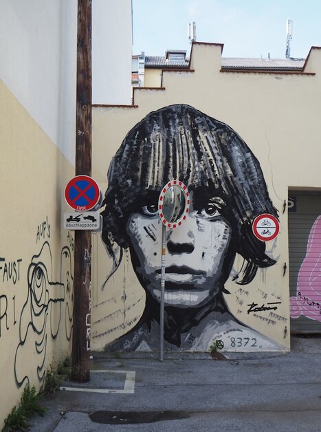 A large mural of a face in Graz, surrounded by traffic signs. | © Elena Paschinger, Creativelena