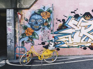 Gelbes Fahrrad vor einer Wand mit farbenfrohem Graffiti von einem Totenkopf und Rosen. | © Adeline Gressin
